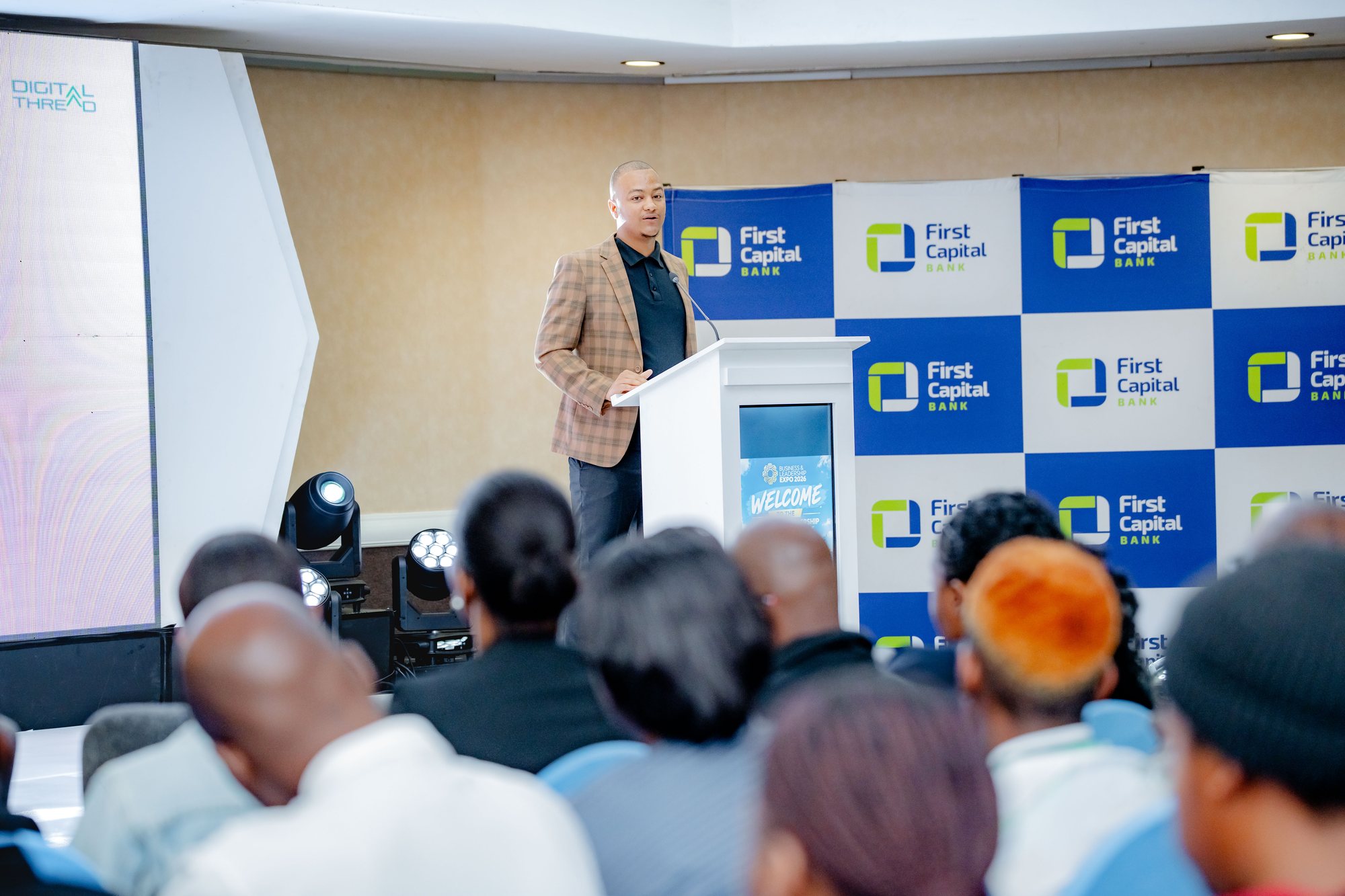 Maverick Kabelo speaking at the lectern with the First Capital Bank backdrop, audience in the foreground