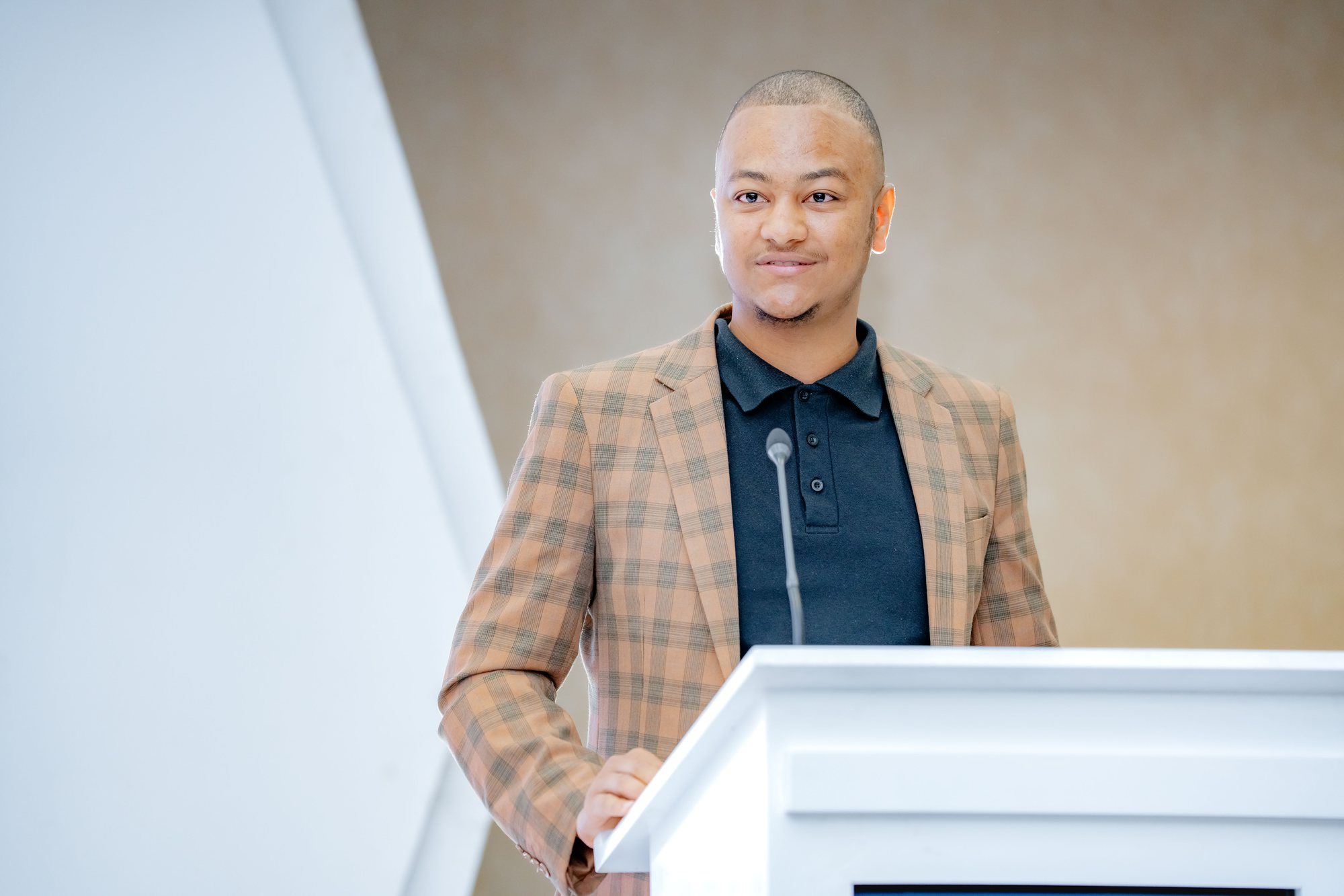 Maverick Kabelo speaking at the lectern, looking toward the screen