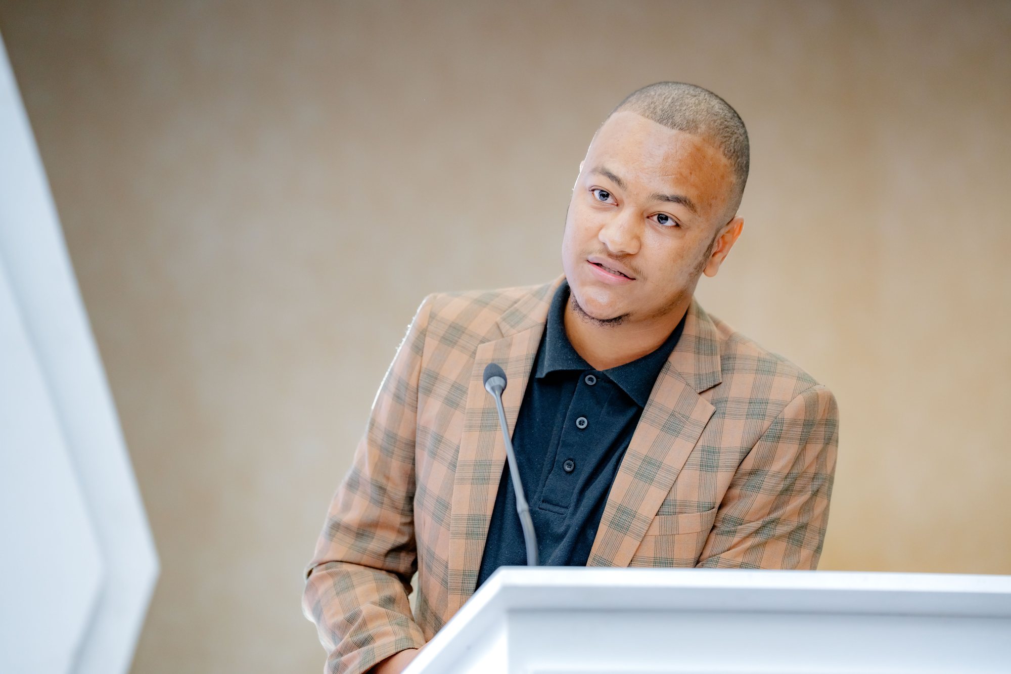 Maverick Kabelo speaking at the lectern, looking toward the screen