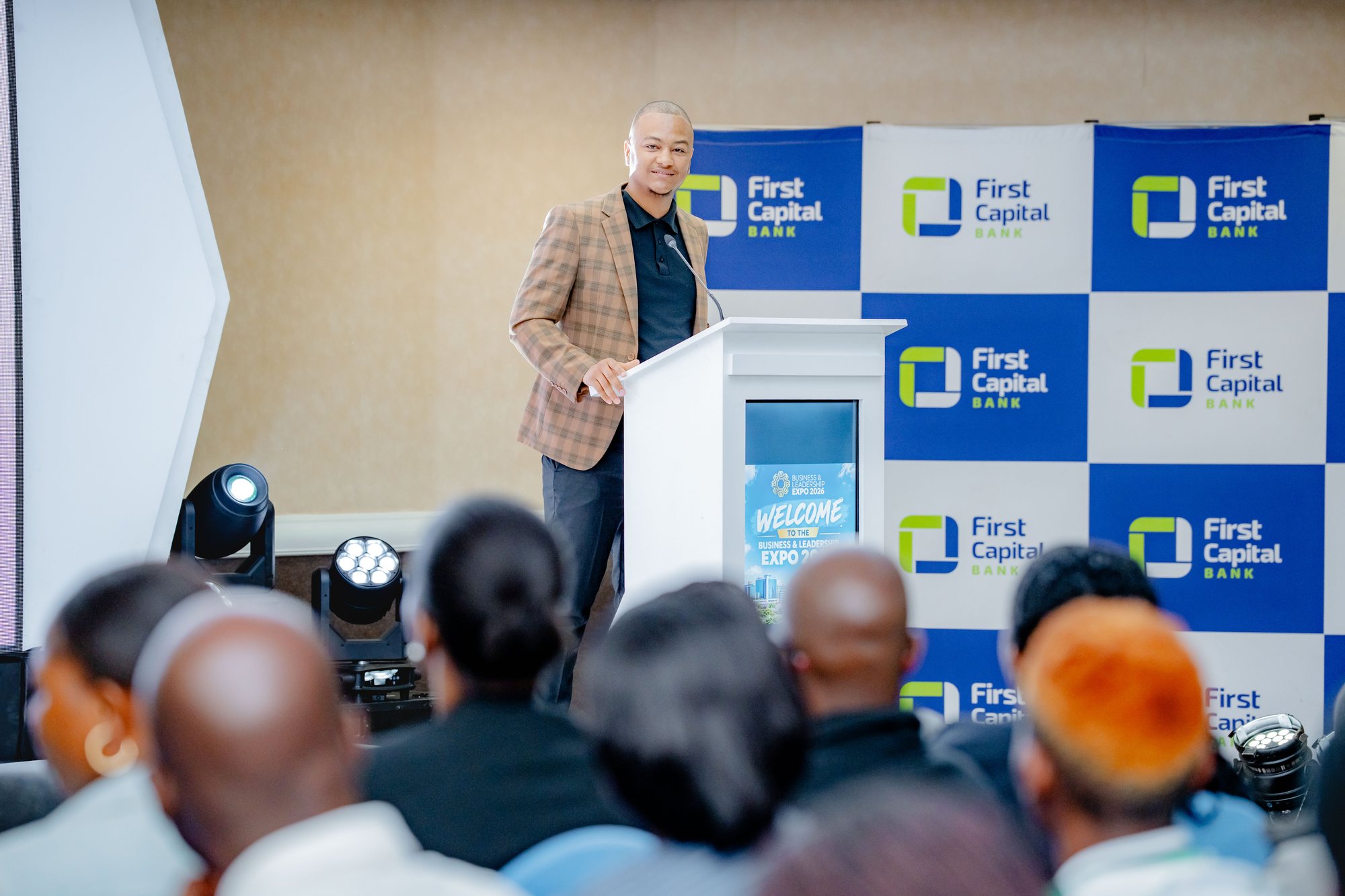 Maverick Kabelo speaking at the lectern, audience seated in the foreground