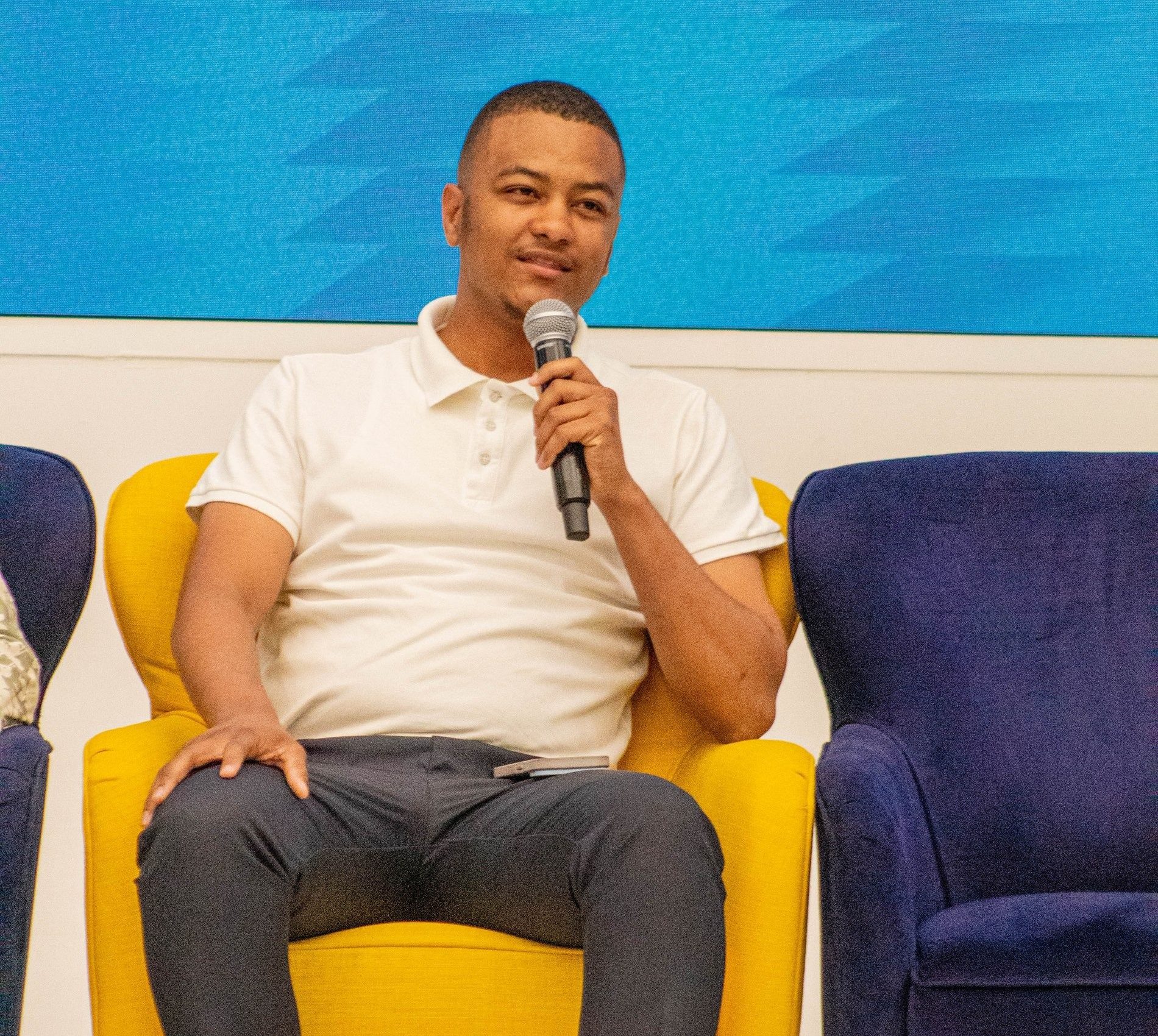 Maverick Kabelo speaking on stage at the Business & Leadership Expo, seated with a microphone